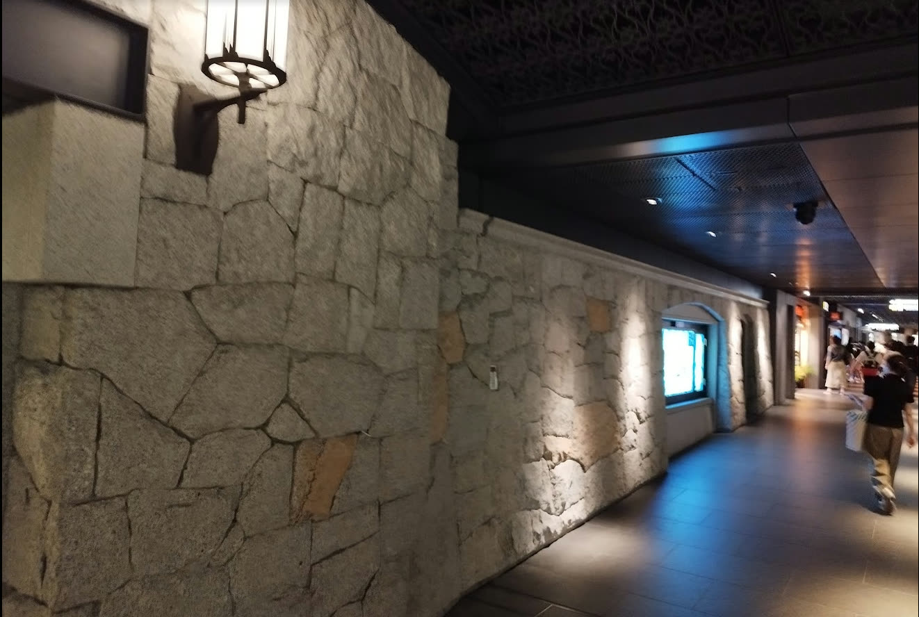 Close-up photo of the stacked-stone wall in the Tenjin underground mall — a granite rampart-style wall continues into the distance, with the lights of modern shops visible beyond