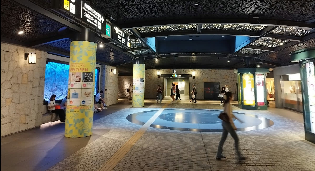 Overview of the "Stone-Paved Plaza" in the Tenjin underground mall — an underground concourse decorated with stacked-stone walls evoking a European castle