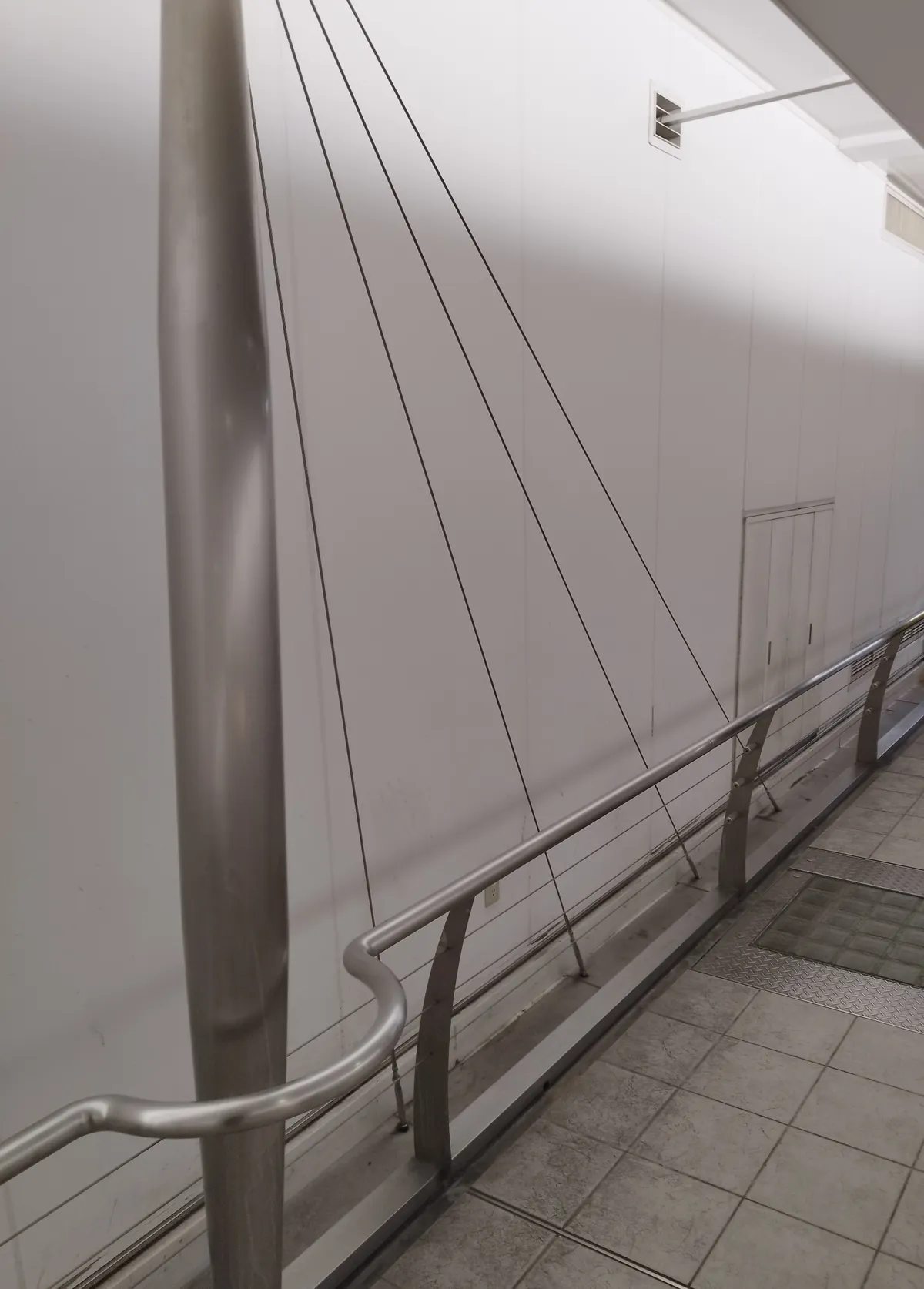Cables stretched across the wall, and a handrail supported by curved metal posts, with a glass-block panel and a metal cover visible in the floor