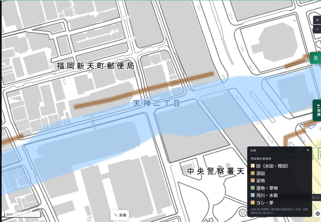 A zoomed-in MAPRISE view around Tenjin 2-chome. A light-blue band indicating a Meiji-era river or waterway cuts diagonally east to west, ignoring today's building blocks