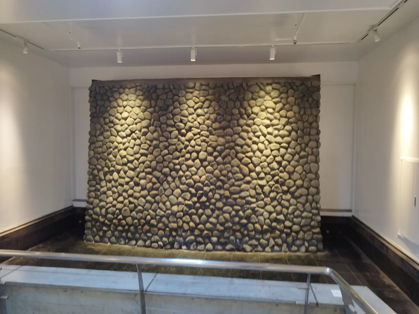 A wall of rounded stones stacked together at the end of the passage, lit by spotlights